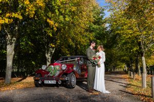 Bride and groom arriving at Applewood Hall in vintage car surrounded by autumn leaves