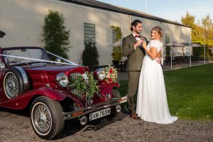 Bride and groom arriving in a ruby red Beauford car