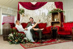 Bride and groom reclining on red baroque sofa with gold sequin backdrop